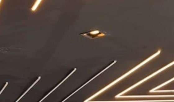 Teto preto do showroom da Empório Motors à noite, com linhas de LED de luz quente que convergem em diagonal e uma luminária embutida