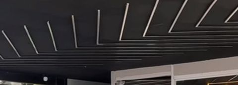 Linhas de LED brancas no teto preto, convergindo sobre a fachada de vidro do showroom